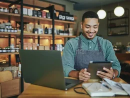 Person working in a store looking at his tablet and having a laptop on a table