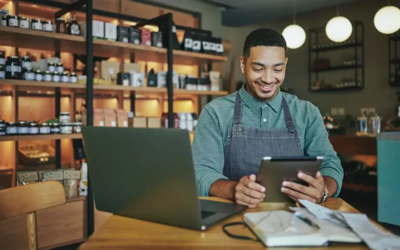 Person working in a store looking at his tablet and having a laptop on a table