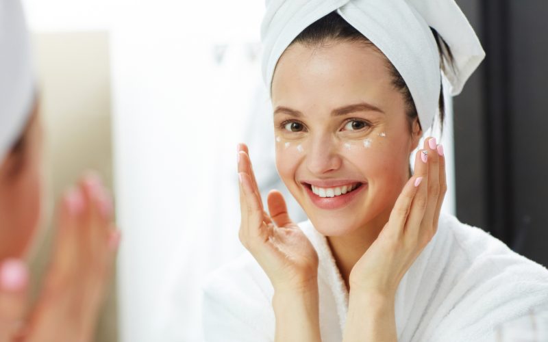 Smiling girl applying cream on her face