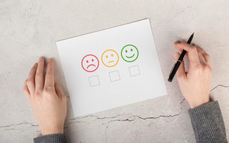 Hands holding a pen over a customer satisfaction survey with three face icons showing different satisfaction levels. A representation of customer service skills