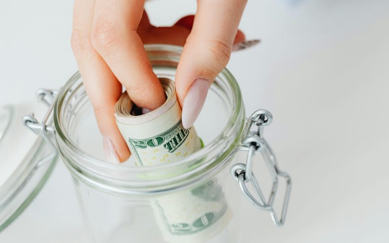 A hand placing rolled-up dollar bills —adding cash to an emergency fund jar